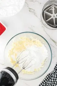 Cream cheese icing ingredients being whipped together in a bowl with an electric mixer - Hostess At Heart