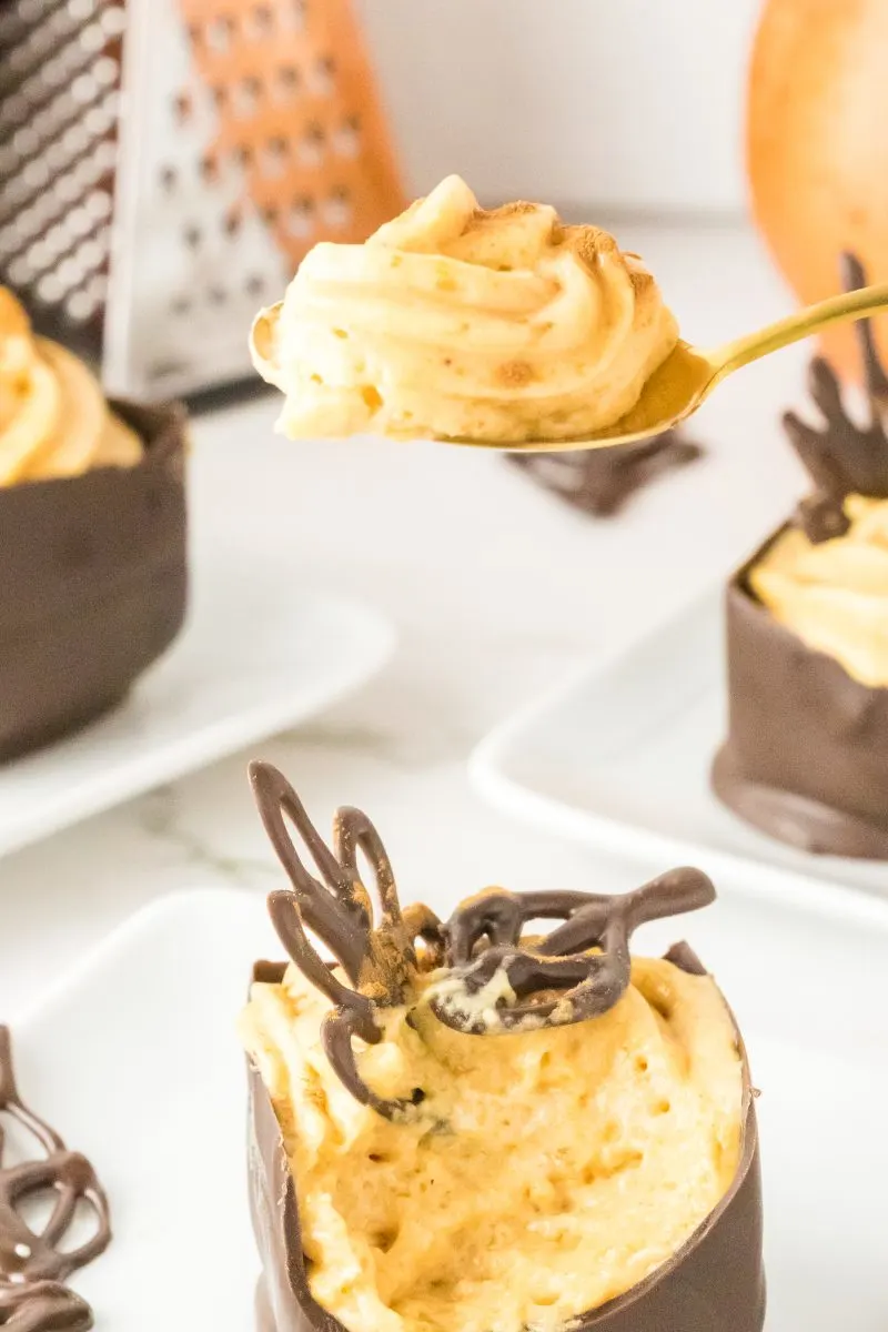 A spoon holding a creamy pumpkin filling over a homemade chocolate cup - Hostess At Heart