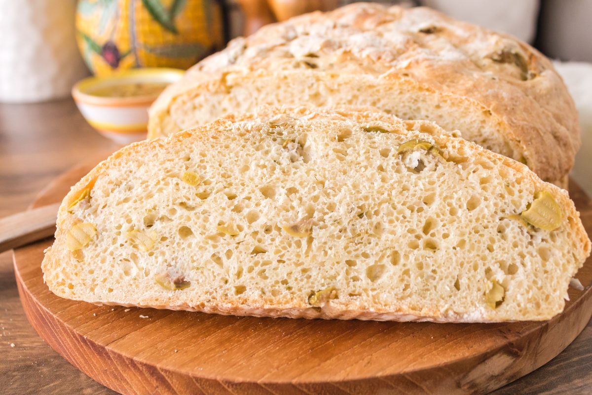 A sideview of a green olive bread loaf with a slice propped up against the front. Hostess At Heart