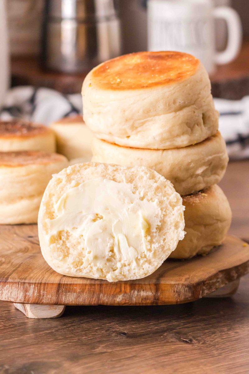Side view of English muffins in a stack with one facing the viewer and covered in cold butter. 