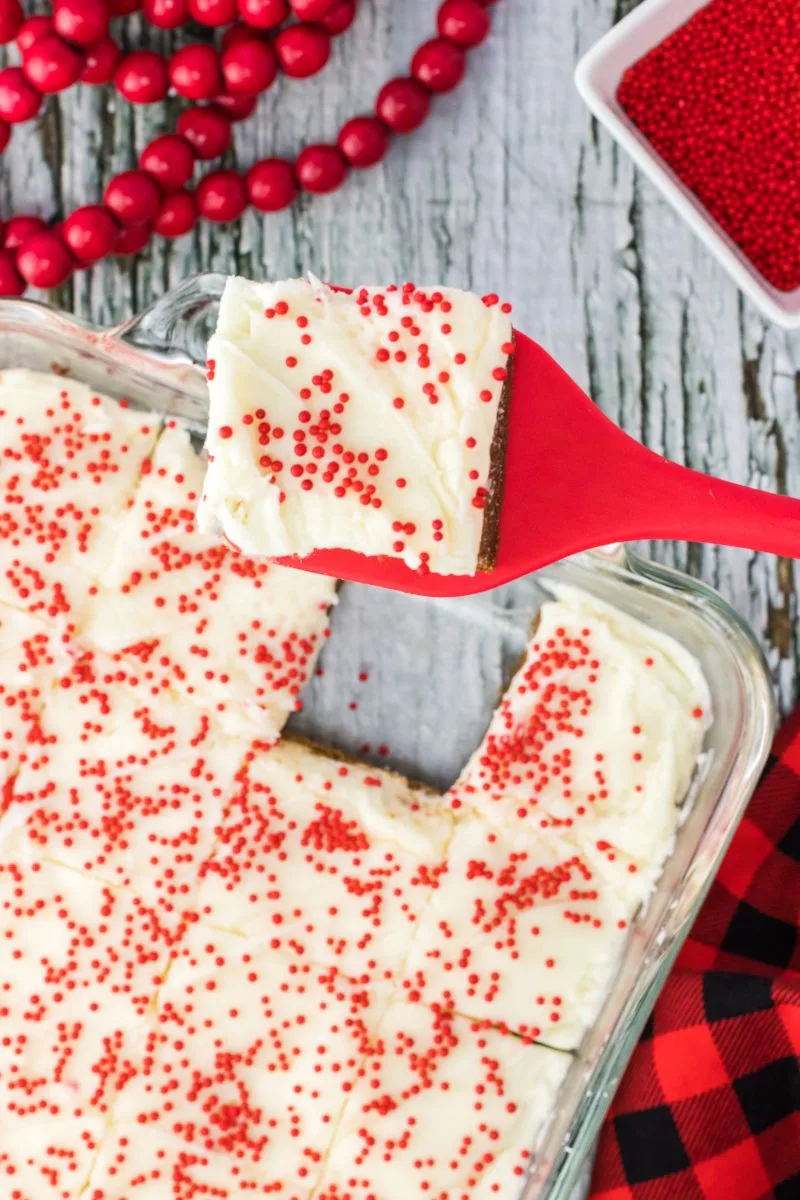 A spatula holding a cut frosted gingerbread cookie bar over the pan of bars - Hostess At Heart