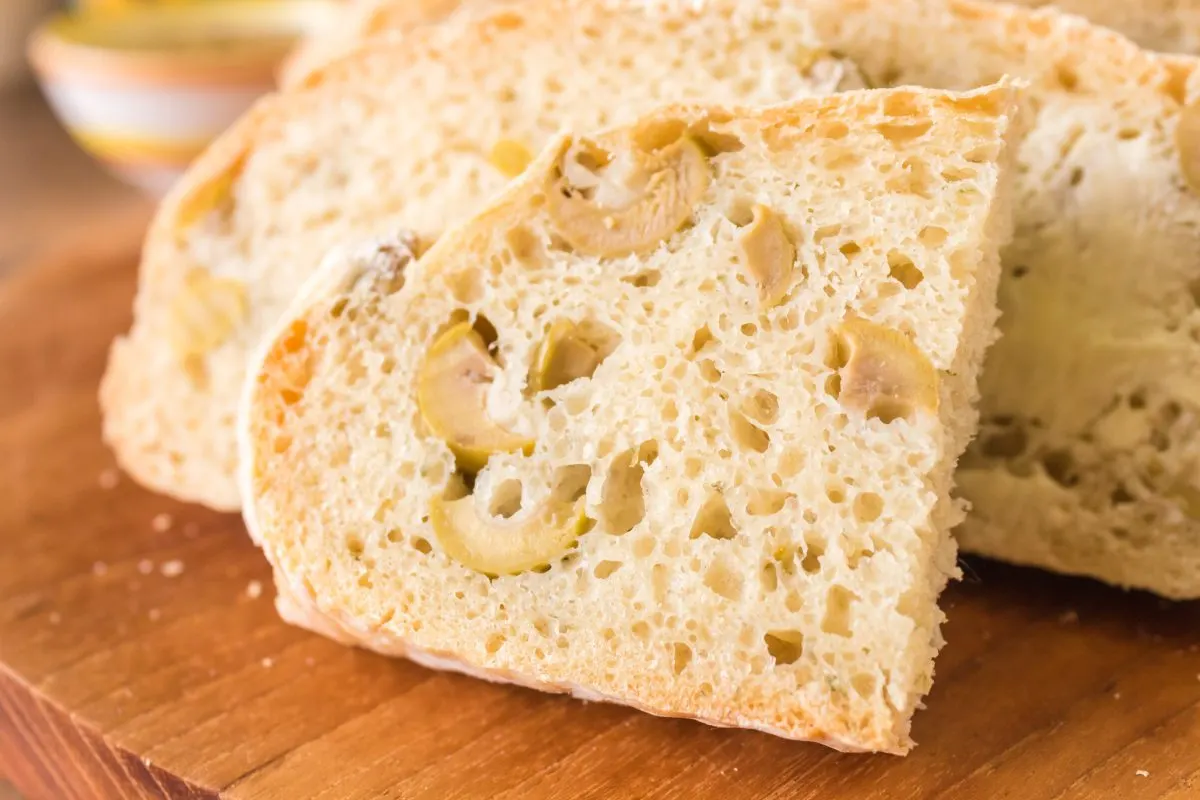 Half a slice of homemade bread dotted with green olives propped up against the loaf. Hostess At Heart