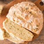 Top down view of a round loaf of olive bread with the front two slices stacked in front of the loaf - Hostess At Heart