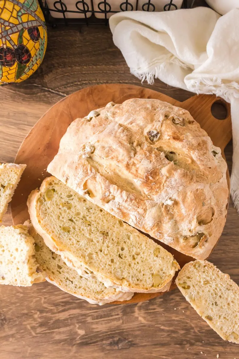 Top down view of slices of green olive bread lying on a cutting board in front of the uncut loaf - Hostess At Heart