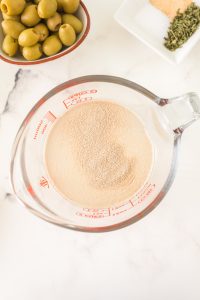 Granulated yeast added to lukewarm water in a measuring cup - Hostess At Heart