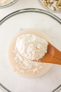 A wooden spoon adding flour to a wet yeast mixture in a bowl. Hostess At Heart