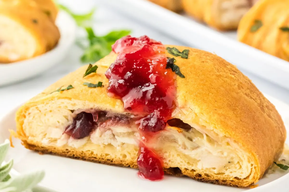 Front view of a sliced Turkey and Cheese Crescent Roll Braid topped with Cranberry Sauce - Hostess At Heart