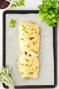 Top down view of braided dough stuffed with turkey and cheese on a parchment paper-lined cookie sheet before baking - Hostess At Heart