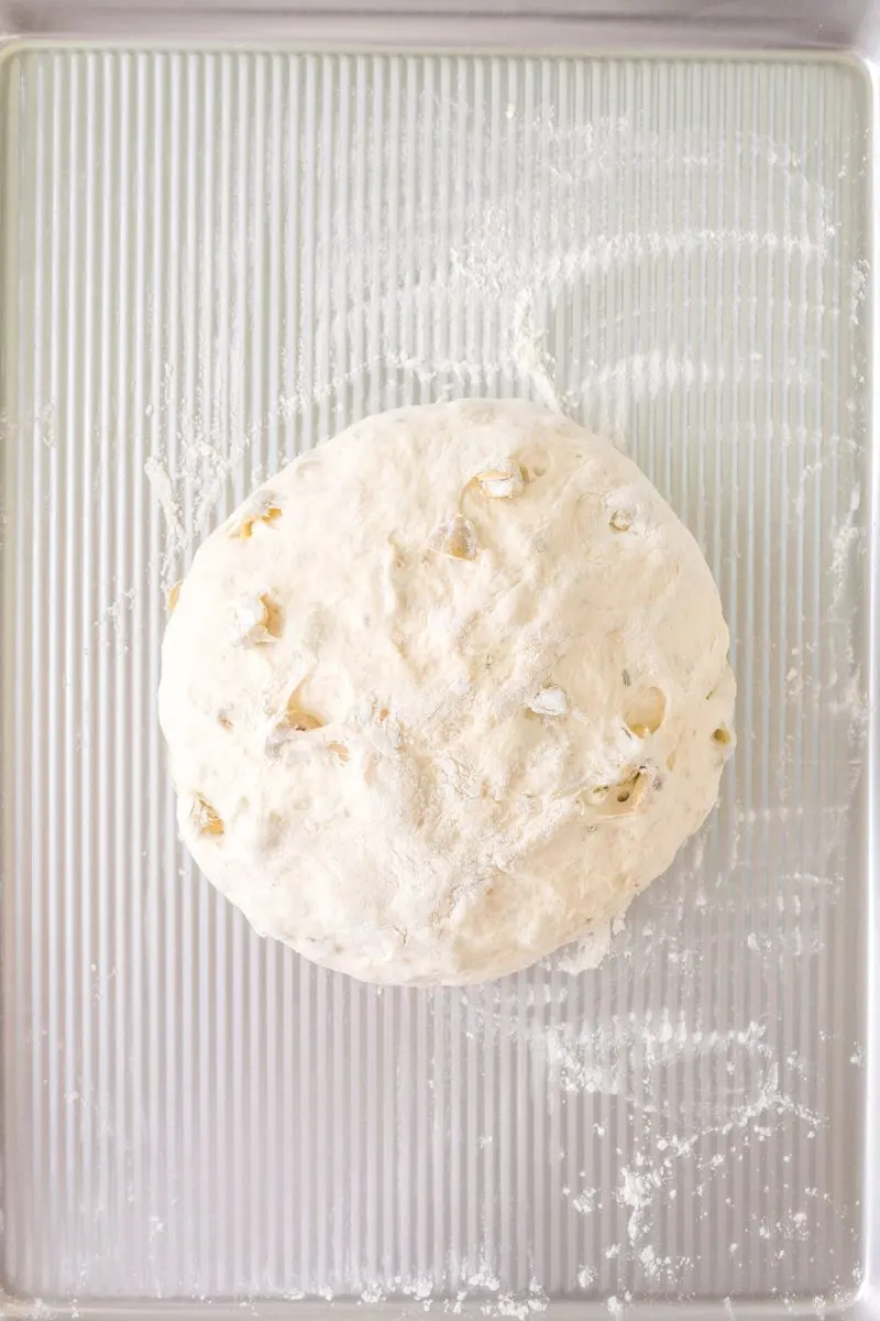 A round shaped loaf of bread sitting on a floured baking sheet - Hostess At Heart