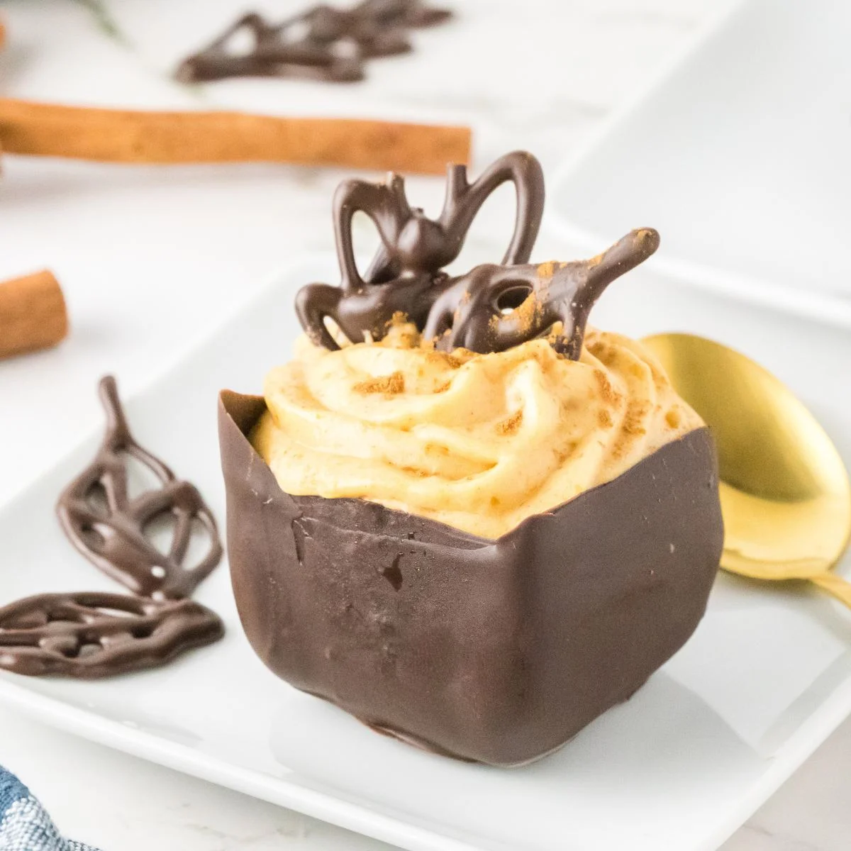 Sideview of an individual chocolate cup filled with piped pumpkin mousse and topped with a decorative chocolate leaf - Hostess At Heart