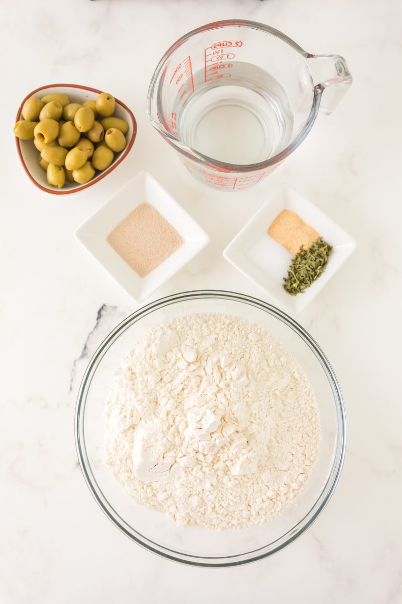 Ingredients used to make homemade olive bread including flour, olives, yeast, water, salt, herbs, and granulated garlic. - Hostess At Heart