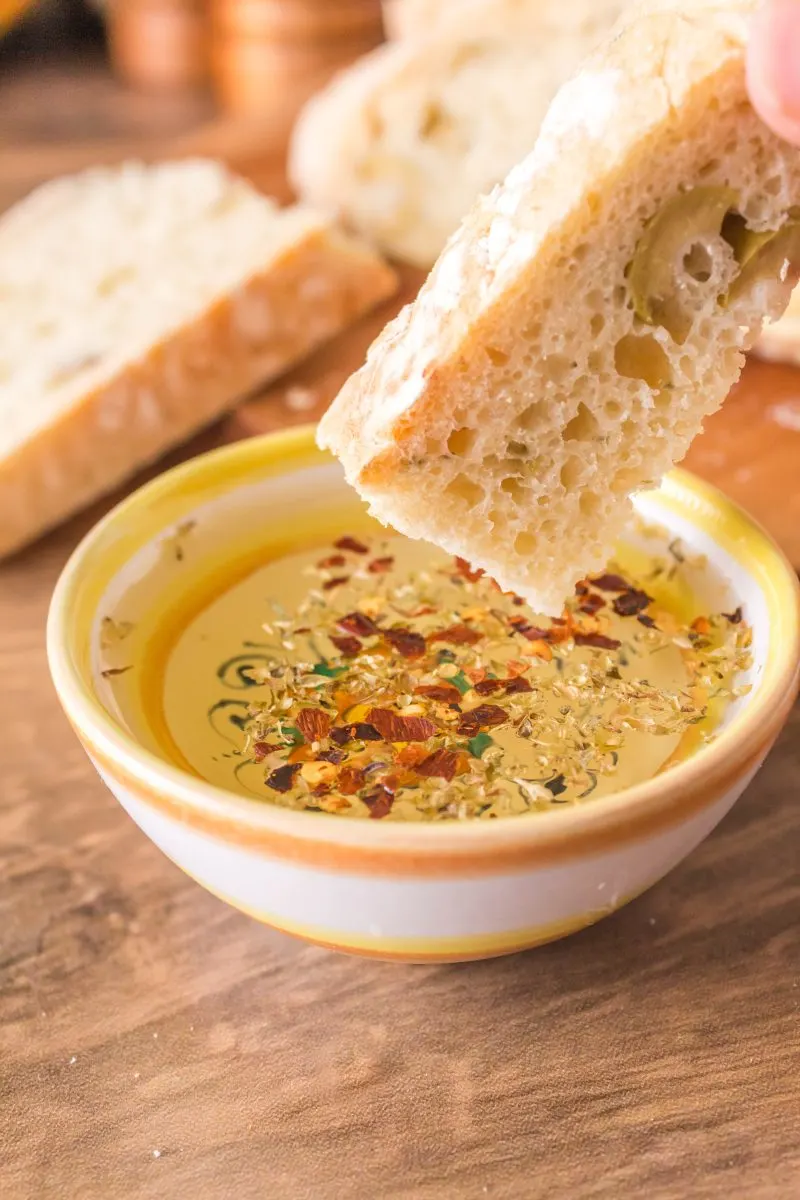 A slice of olive bread being dipped into a bowl of spiced olive oil. Hostess At Heart