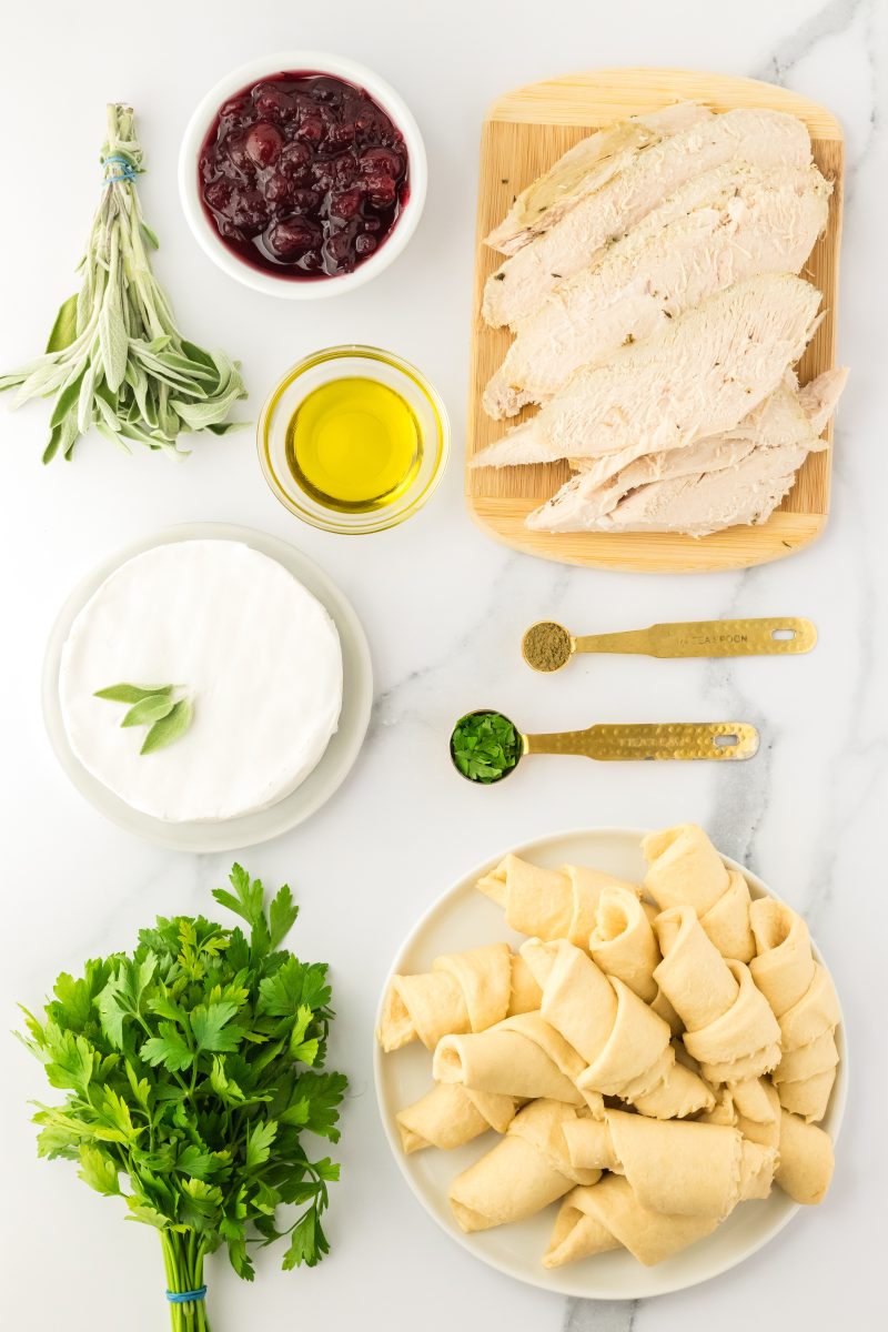 Turkey Roll ingredients needed to make a crescent braid including canned crescent roll, sliced turkey, olive oil, cranberry sauce, brie, and herbs