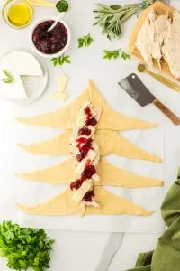 Crescent roll dough laid out and topped with slices of turkey, brie, and cranberry sauce - Hostess At Heart