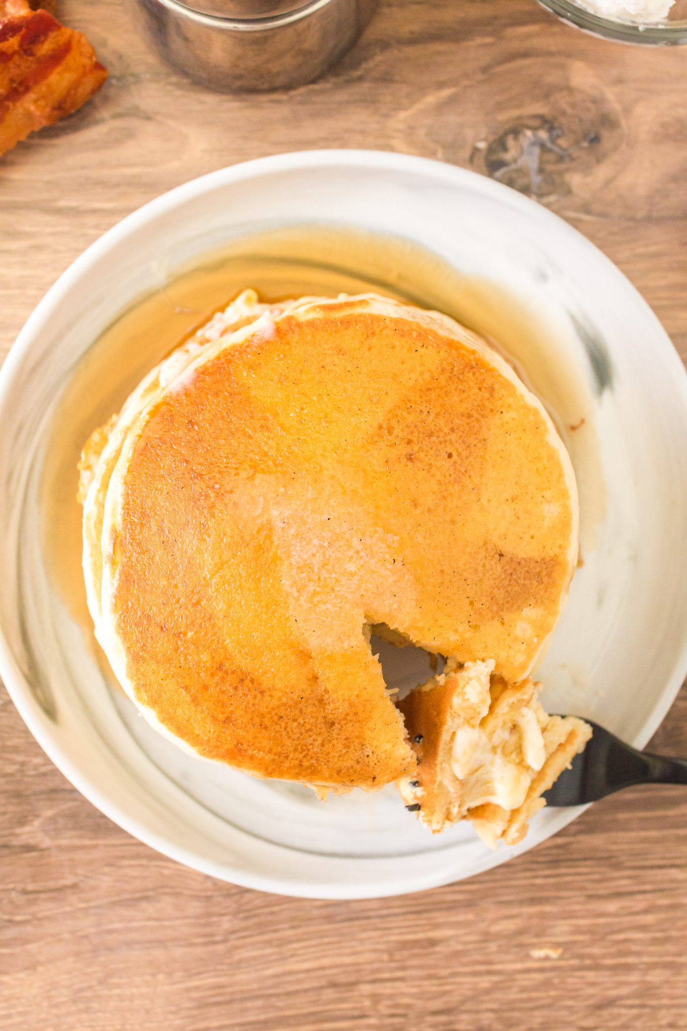 Top down view of a stack of fluffy golden brown sourdough pancakes with a fork lifting a bite - Hostess At Heart
