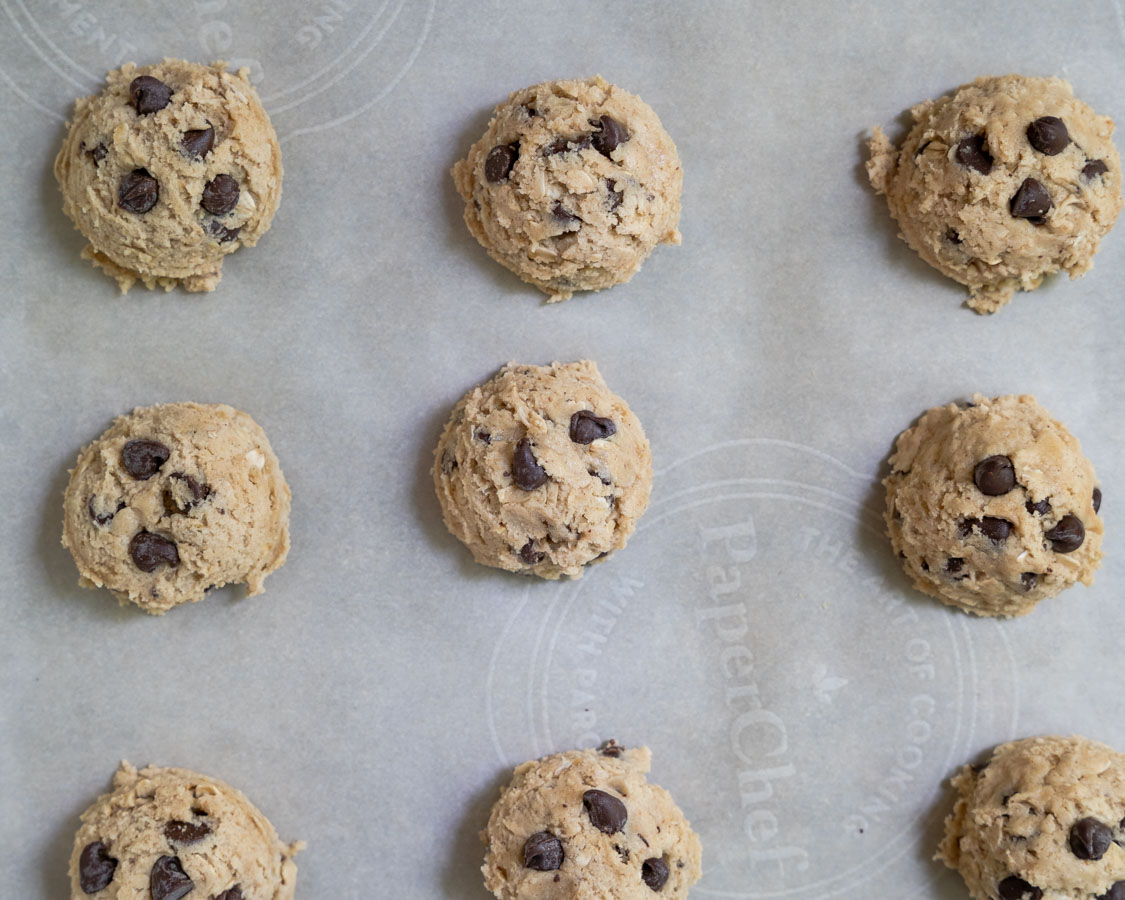 Scooped balls of dough with chocolate chips pressed into the top on a cookie sheet - Hostess At Heart
