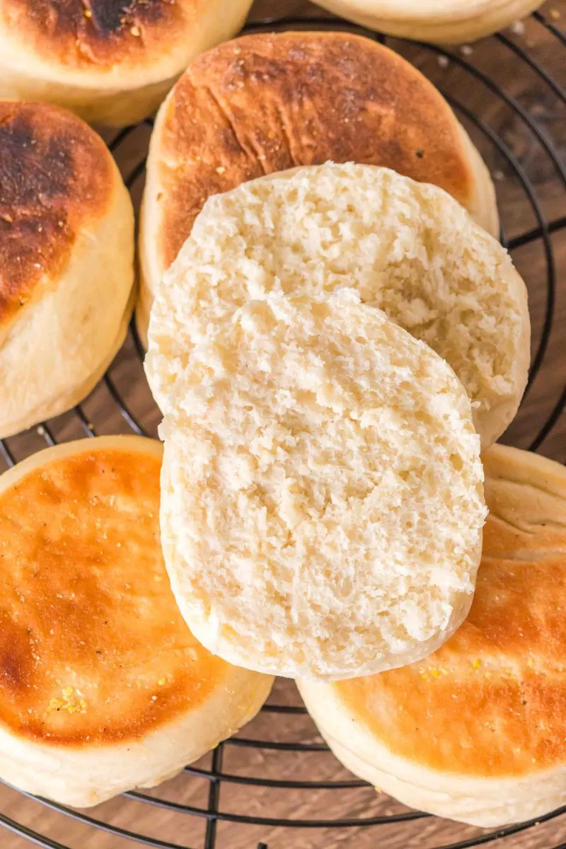 Golden brown english muffins sitting on a cooling rack with the top one cut in half - Hostess At Heart