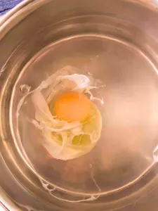 An egg in a hot water filled saucepan that's beginning to poach - Hostess At Heart