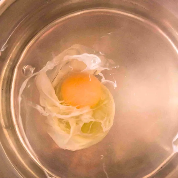 An egg in a hot water filled saucepan that's beginning to poach - Hostess At Heart