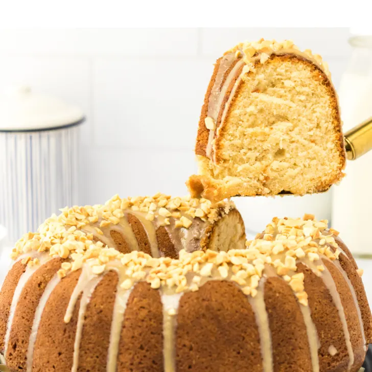 A slice of cake lifted from a baked peanut butter bundt cake topped with glaze and chopped peanuts - Hostess At Heart
