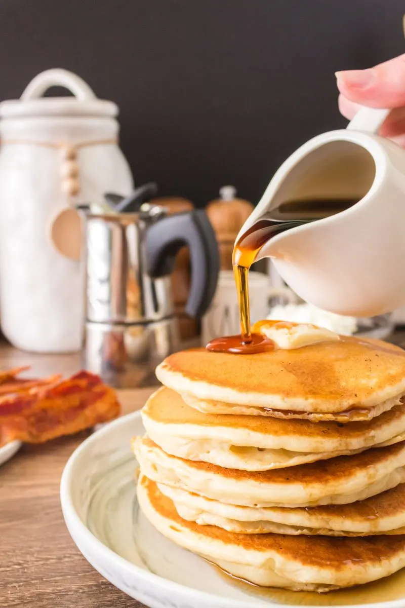 A stack of Sourdough Discard Pancakes with syrup being poured over the top. Hostess At Heart