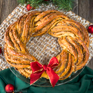 Top down view of a twisted cinnamon bread dough shaped into a wreath and garnished with a read bow - Hostess At Heart