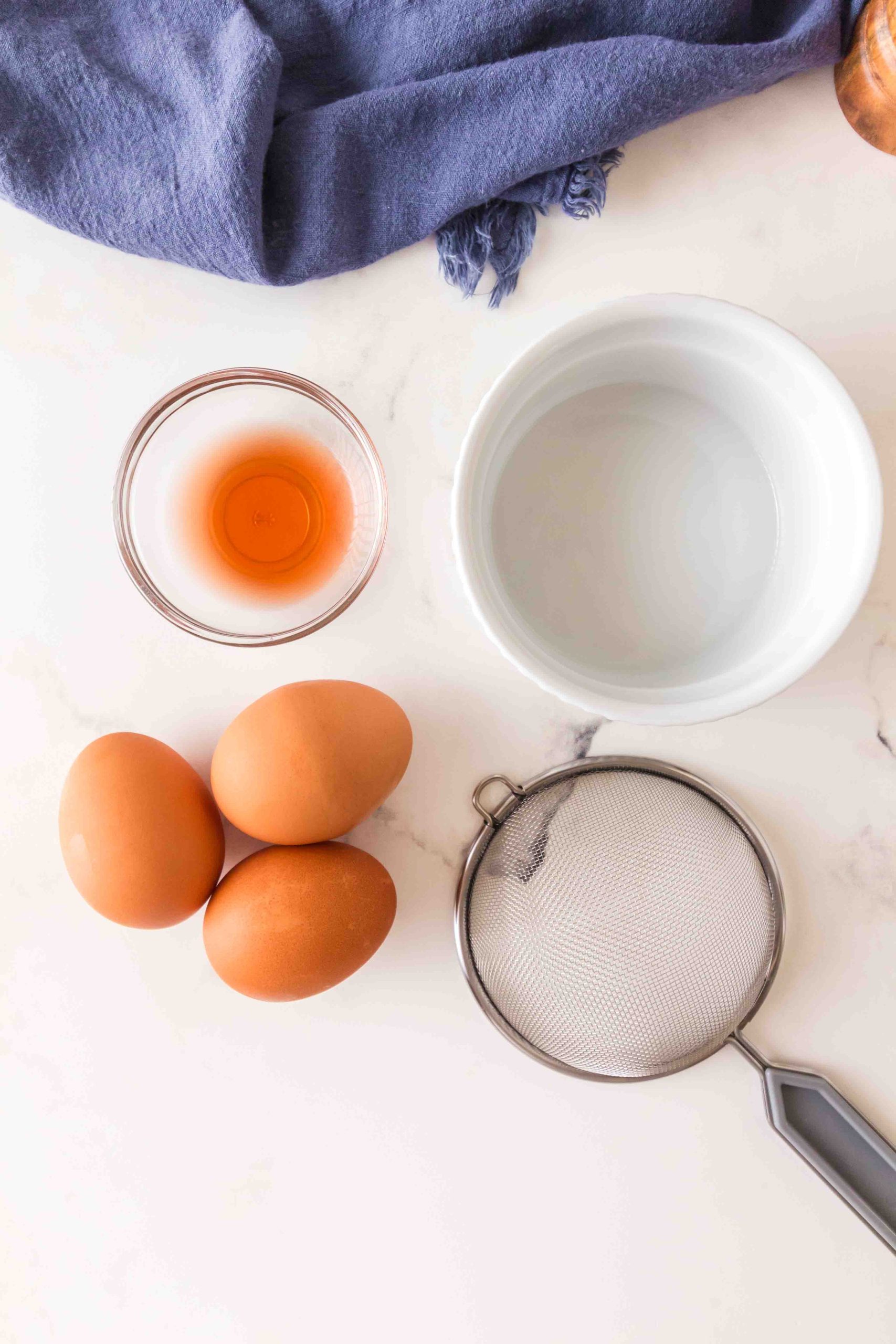Equipment used to make poached eggs including fine mesh seive and a ramekin next to some uncooked eggs.
