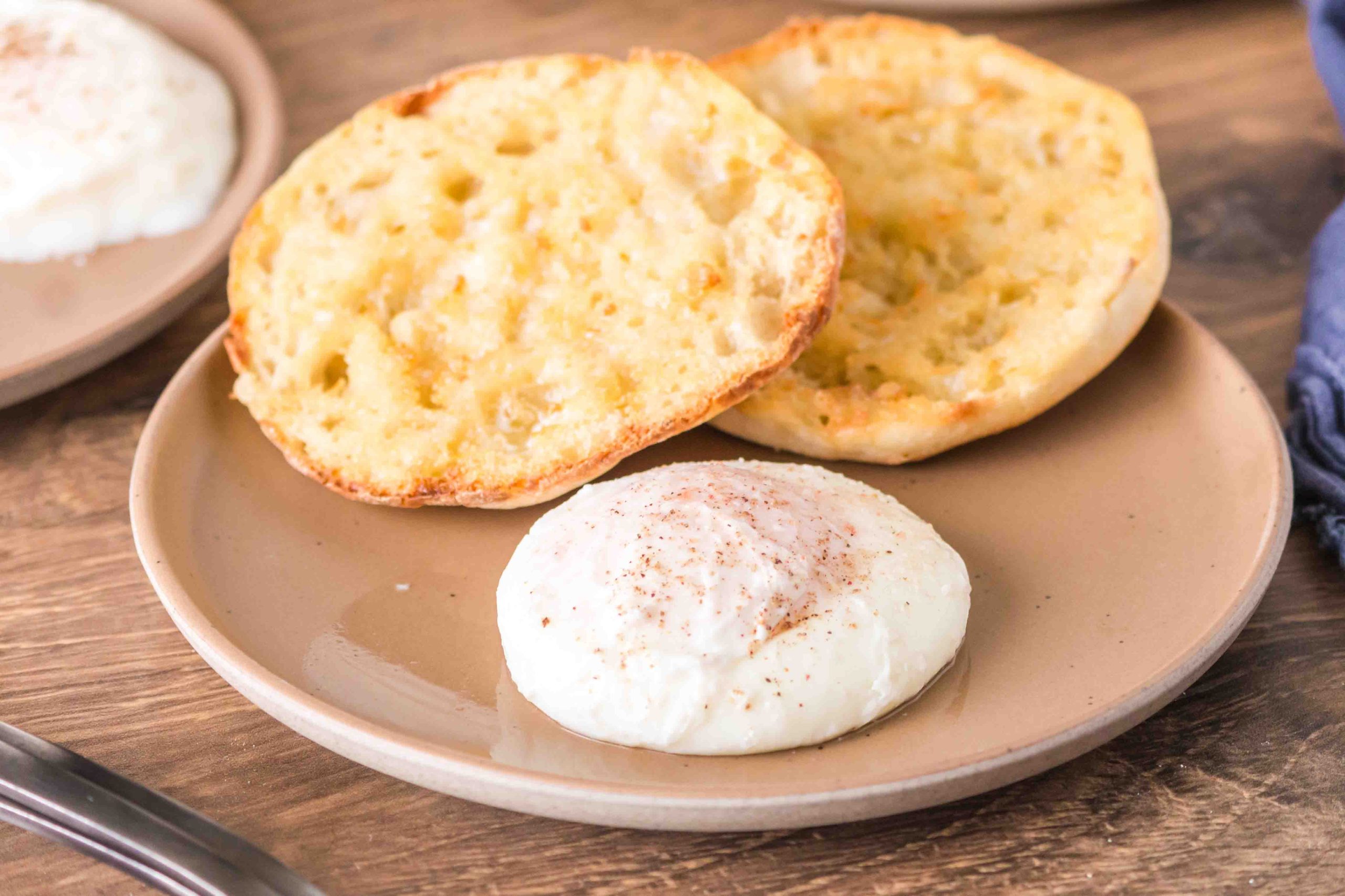 A beautifully poached egg on a plate in front of a split and toasted English Muffin - Hostess At Heart