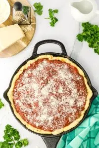 A cast-iron skillet filled with layers of dough, cheese, sauce and a sprinkle of Parmesan - Hostess At Heart