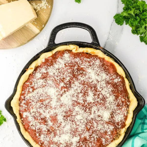 A cast-iron skillet filled with layers of dough, cheese, sauce and a sprinkle of Parmesan - Hostess At Heart