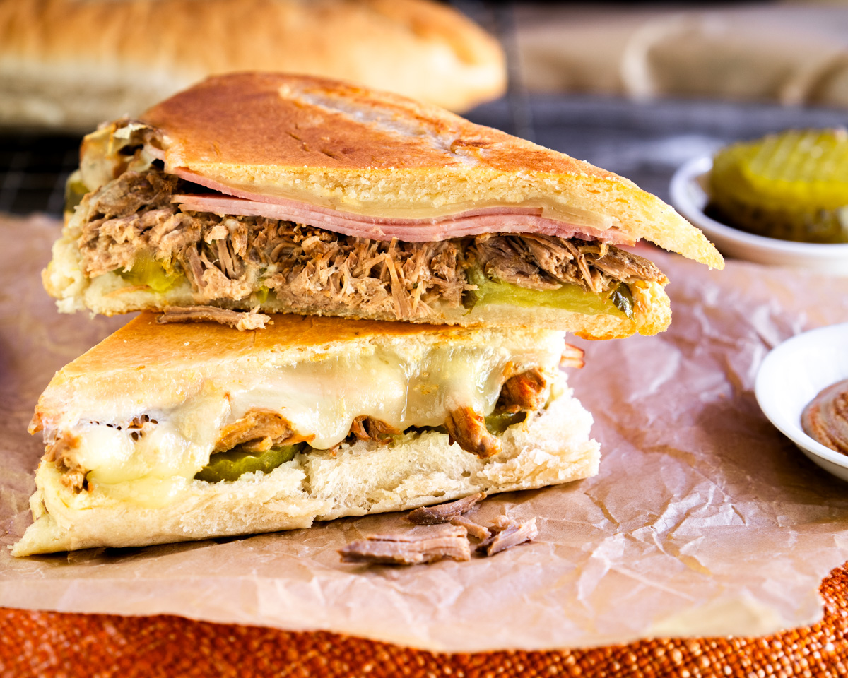 Sideview of the Best Cuban Sandwich loaded with shredded pork, sliced ham, Swiss cheese, and mustard pressed together in cuban bread. Hostess At Heart