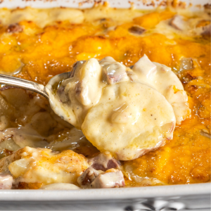 A spoon lifting a serving of cheesy Au Gratin Potatoes and Corned Beef from a casserole dish. Hostess At Heart