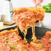 A slice of pizza dripping with melted cheese being lifted out of a cast-iron pan holding the rest of the pizza - Hostess At Heart