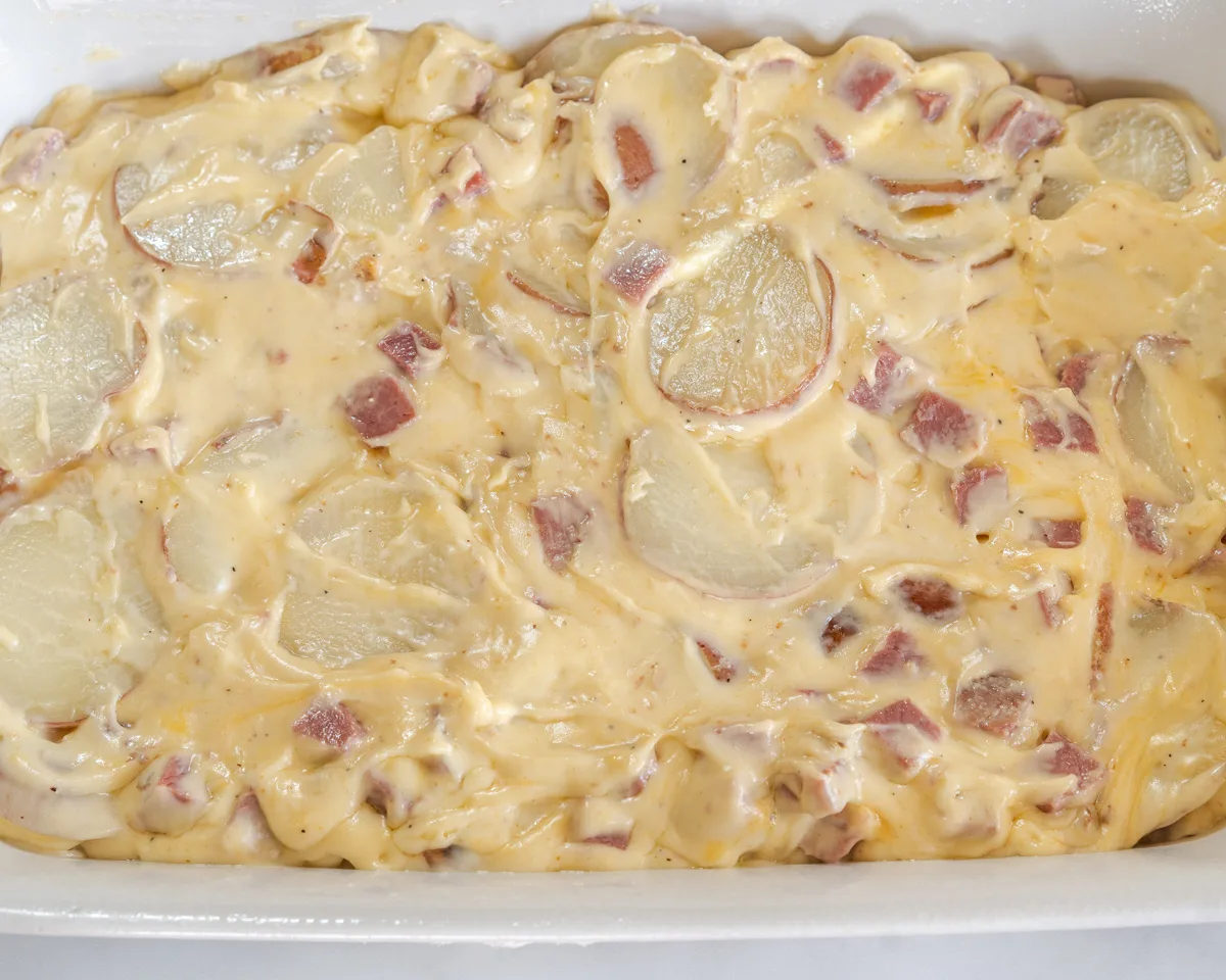 A casserole dish filled with sliced potatoes and diced corned beef in a thick cheesy sauce. Hostess At Heart