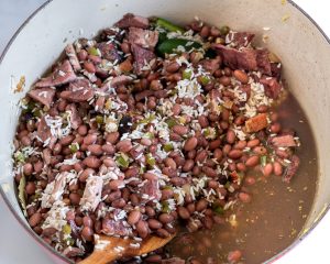 A Dutch oven filled with broth, red beans, spices, rice, and chunks of ham for Cuban Red Bean soup - Hostess At Heart