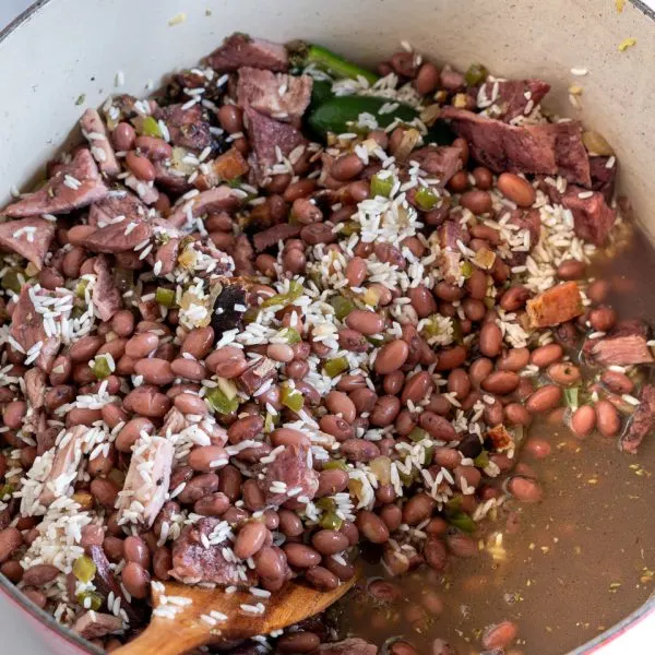 A Dutch oven filled with broth, red beans, spices, rice, and chunks of ham for Cuban Red Bean soup - Hostess At Heart