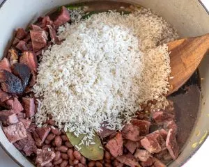 Parboiled rice added to a Dutch oven filled with Cuban Congri ingredients - Hostess At Heart