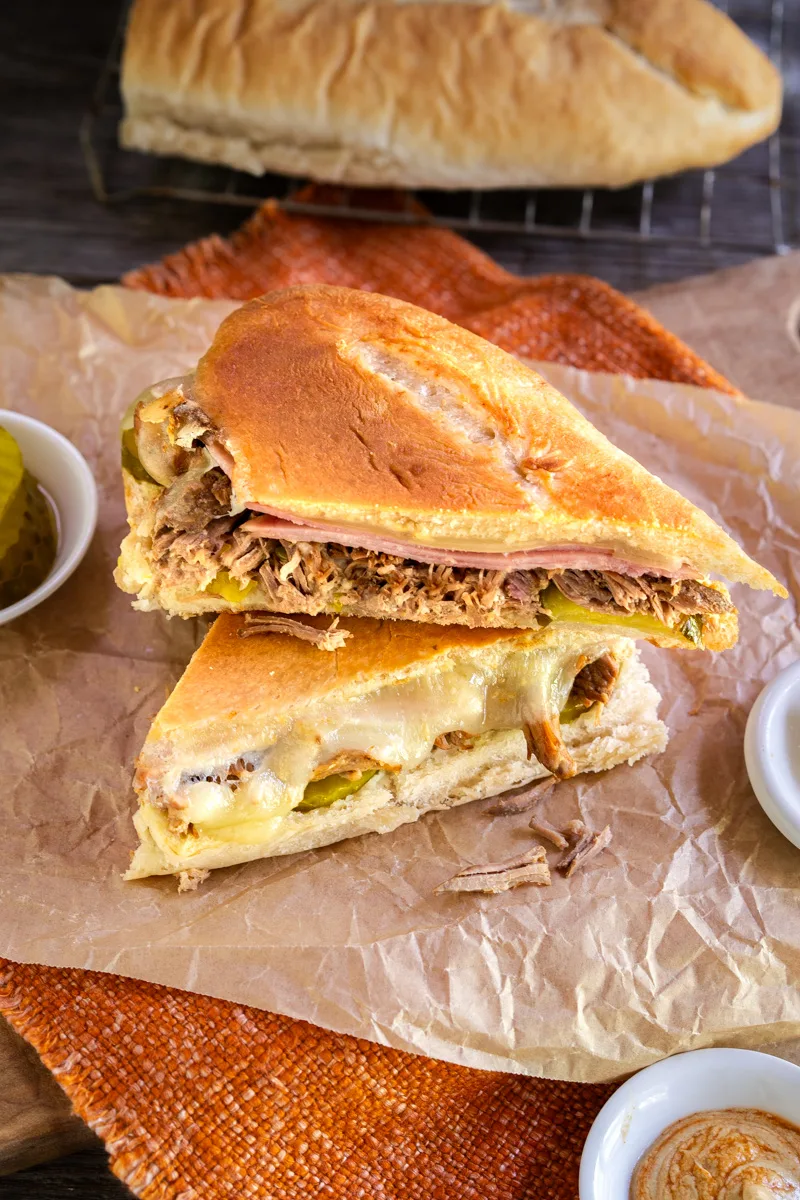 Sideview of a sliced sandwich loaded with Cuban shredded pork, Swiss Cheese, ham slices, pickles, and mustard - Hostess At Heart