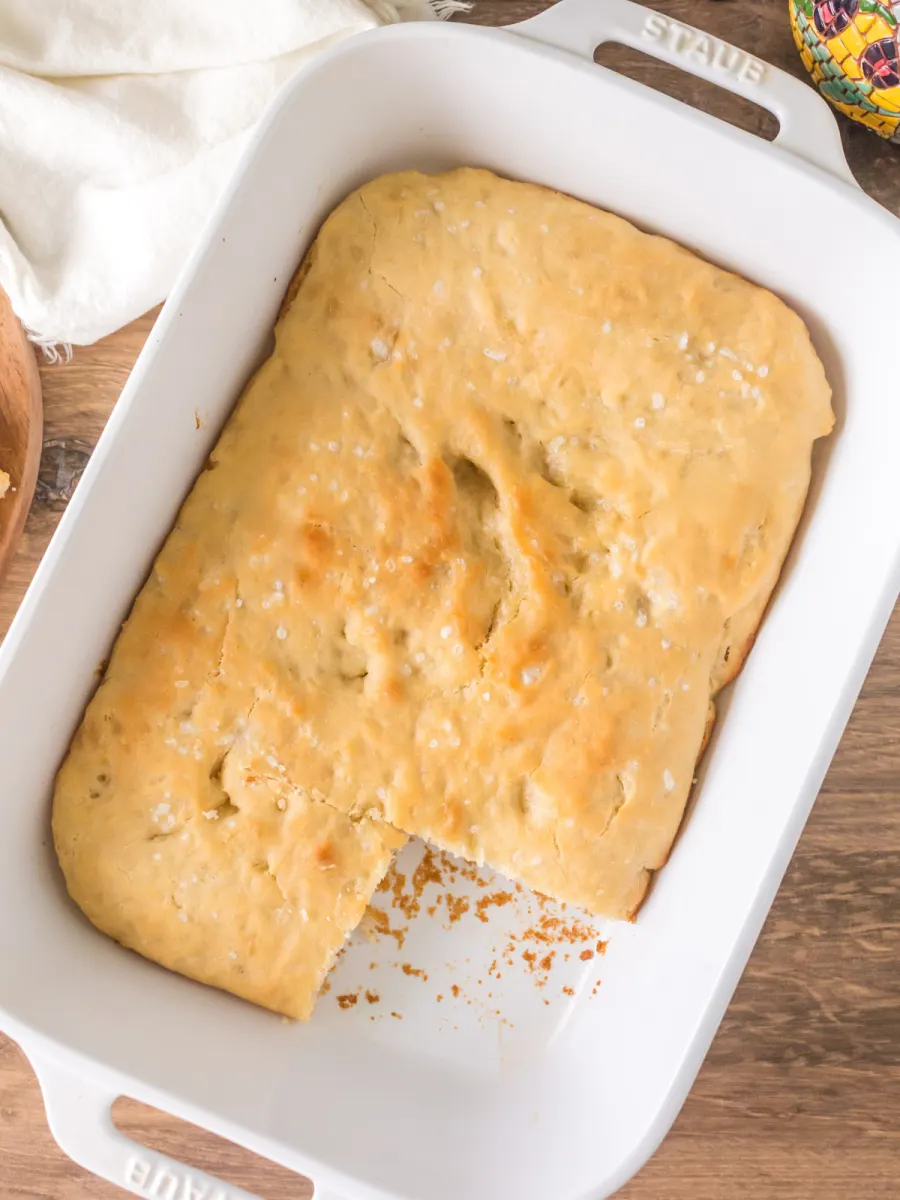 Top down view of a pan of baked focaccia sourdough bread with a piece missing - Hostess At Heart