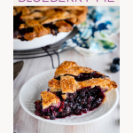 Sideview image for Pinterest of a slice of homemade blueberry pie with a lattice crust sitting on a serving plate. Hostess At Heart
