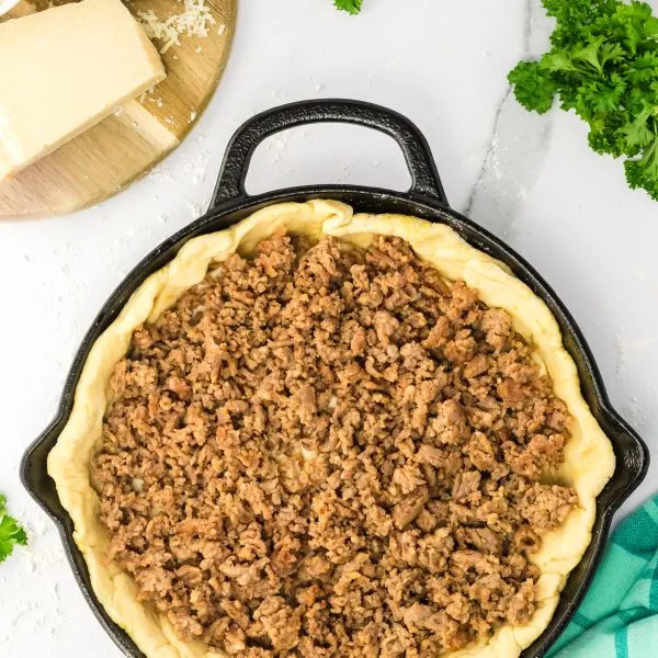 Browned sausage over a layer of pizza dough in a cast-iron skillet - Hostess At Heart