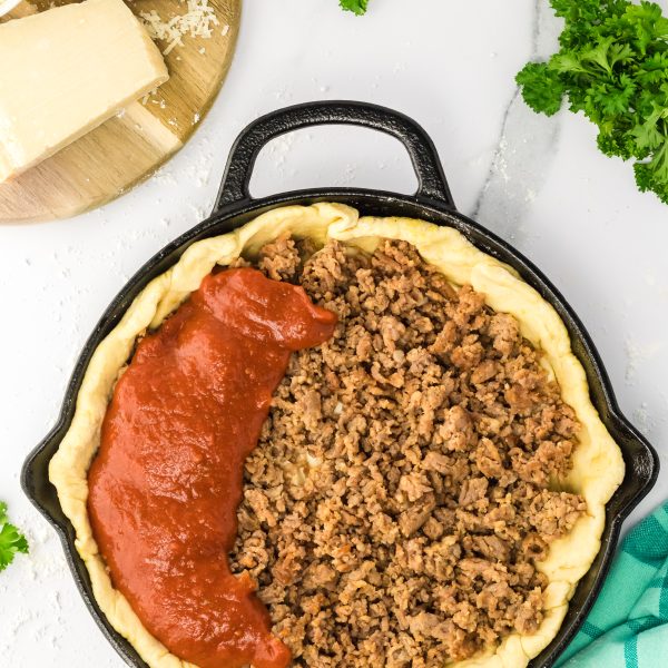 Cast Iron skillet lined with pizza dough and layers of ground sausage and sauce - Hostess At Heart