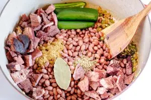 A dutch oven filled with ham chunks, soaked bbeans, spices, and peppers
