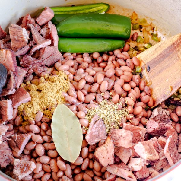 A dutch oven filled with ham chunks, soaked bbeans, spices, and peppers