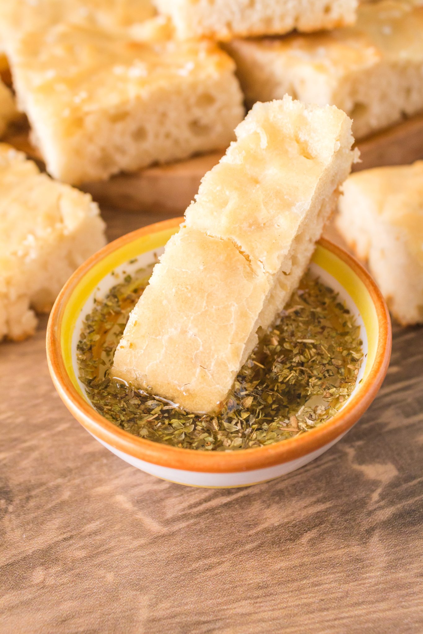 A slice of bread dipped into a bowl filled with olive oil and spices - Hostess At Heart