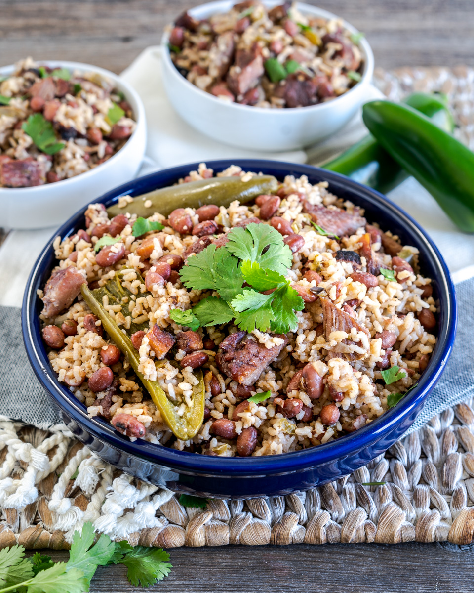 A serving bowl filled with Cuban Red Beans and Rice, garnished with cooked jalapenos and fresh cilantro - Hostess At Heart