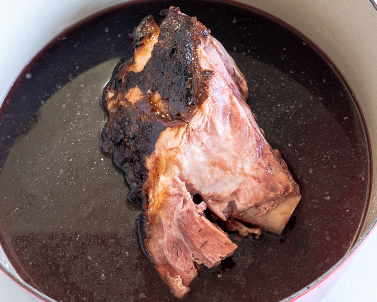 A ham shank sitting in a Dutch oven filled with liquid. - Hostess At Heart