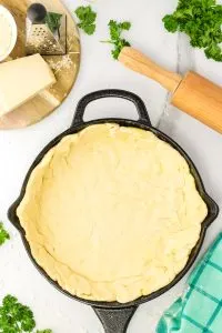 Pizza dough layered over the bottom and up the sides of a cast iron skillet. Hostess At Heart