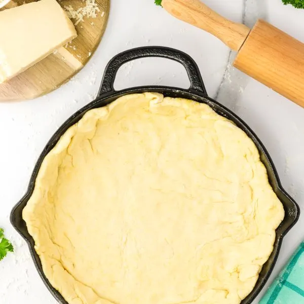 Pizza dough layered over the bottom and up the sides of a cast iron skillet. Hostess At Heart