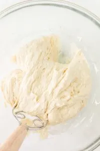 A Danish whisk pulling bread dough from the top of the bowl towards the bottom of the bowl - Hostess At Heart